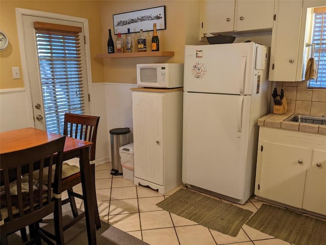 kitchen with tile counters, white appliances, light tile patterned floors, a wainscoted wall, and white cabinets