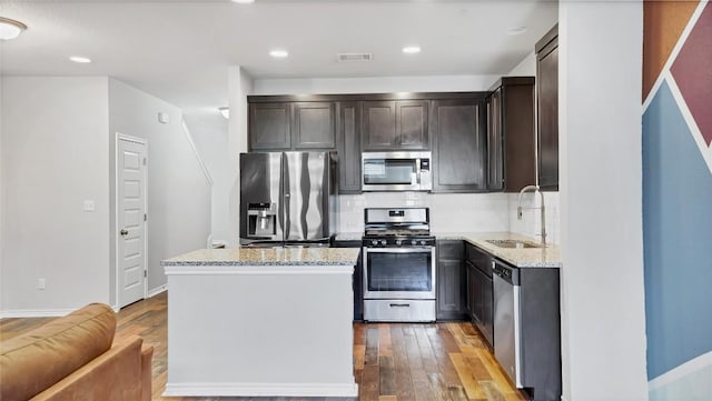 1837 Artesian Springs Xing, Leander, TX 78641 - kitchen with wood finished floors, a sink, a kitchen island, light stone countertops, and appliances with stainless steel finishes