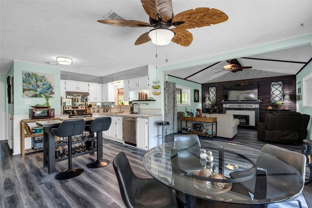 dining area featuring a textured ceiling, lofted ceiling with beams, ceiling fan, a fireplace, and dark wood-style floors