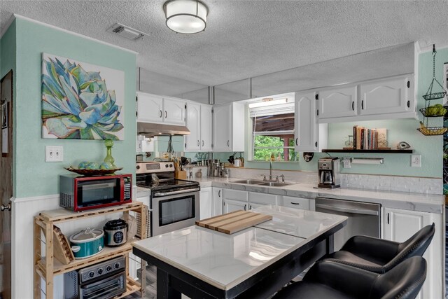 kitchen with a sink, a textured ceiling, appliances with stainless steel finishes, white cabinets, and under cabinet range hood