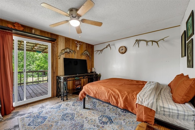 bedroom with wooden walls, a textured ceiling, ceiling fan, and access to exterior