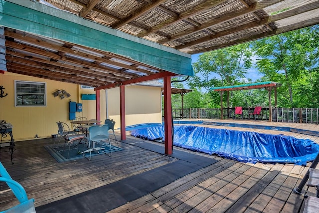 view of pool featuring a covered pool, a wooden deck, fence, and outdoor dining space