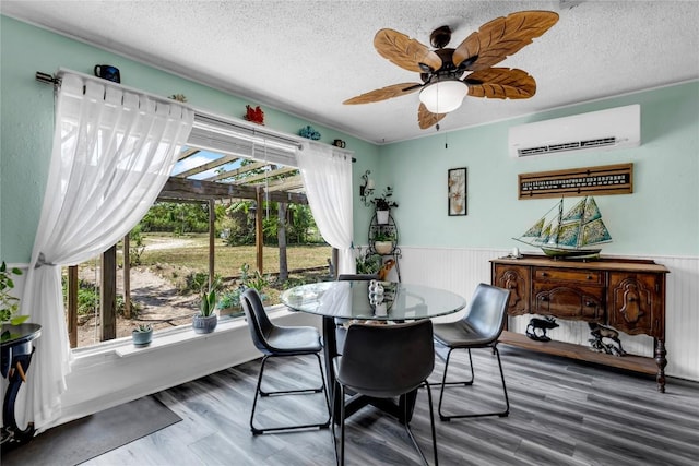 dining area with a wall mounted air conditioner, a wainscoted wall, wood finished floors, and a textured ceiling