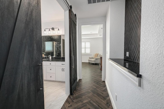 hall with visible vents, a textured wall, baseboards, and a barn door