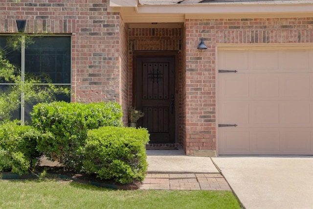 entrance to property with brick siding, an attached garage, and driveway