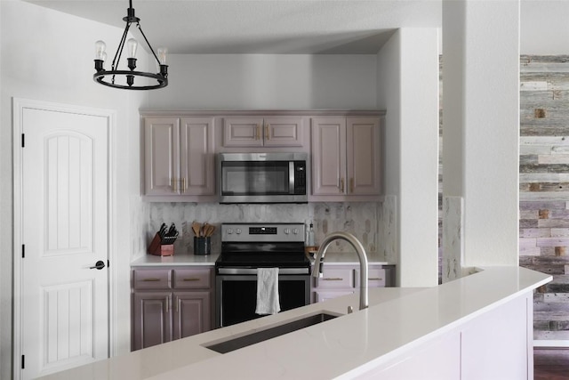kitchen featuring light countertops, a sink, decorative backsplash, appliances with stainless steel finishes, and a notable chandelier