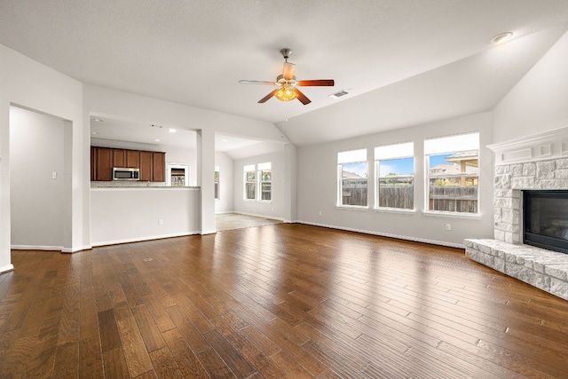 unfurnished living room featuring dark wood finished floors, a stone fireplace, visible vents, vaulted ceiling, and ceiling fan