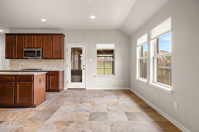 kitchen with vaulted ceiling, baseboards, stainless steel microwave, backsplash, and stone finish floor