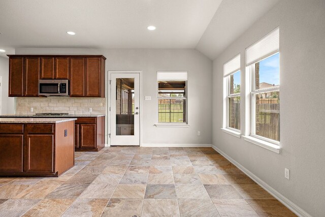 1512 Daylily Loop, Georgetown, TX 78626 - kitchen featuring stainless steel microwave, decorative backsplash, light stone finish floors, baseboards, and lofted ceiling