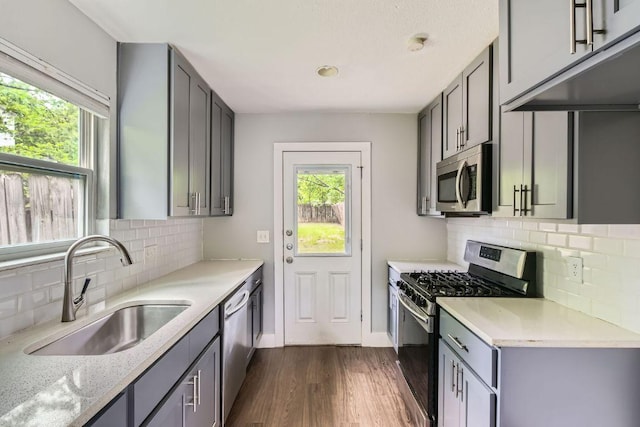 kitchen featuring dark wood-style floors, stainless steel appliances, a sink, decorative backsplash, and gray cabinetry