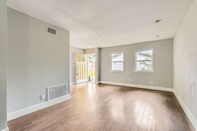 spare room featuring baseboards, visible vents, a textured ceiling, and wood-type flooring