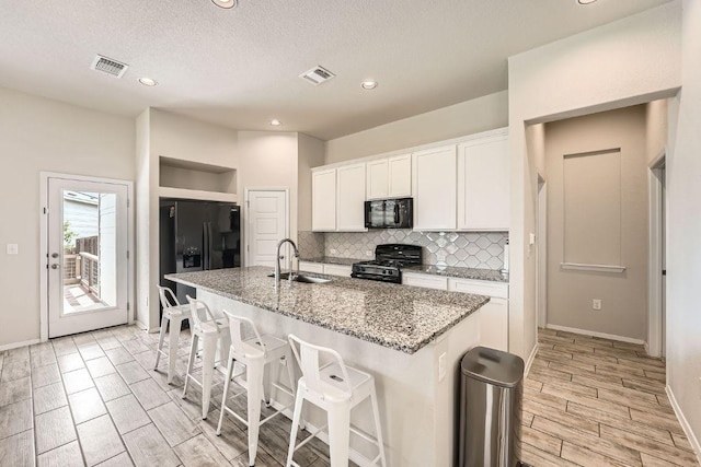 11509 Brindle Ct, Manor, TX 78653 - kitchen featuring black appliances, a sink, backsplash, white cabinets, and a kitchen island with sink