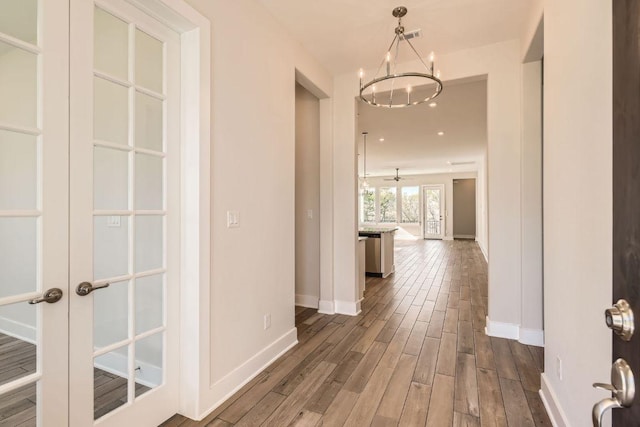 hallway with french doors, baseboards, an inviting chandelier, and dark wood finished floors