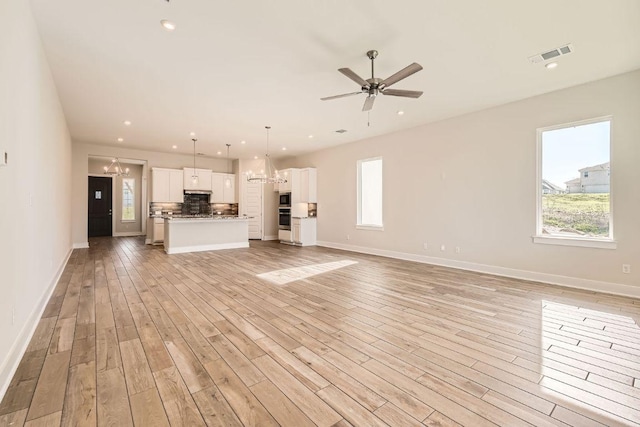 unfurnished living room with light wood-type flooring, plenty of natural light, visible vents, and ceiling fan with notable chandelier