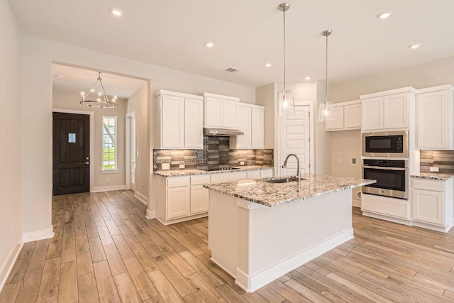 kitchen featuring stainless steel oven, light wood-style flooring, under cabinet range hood, and a sink