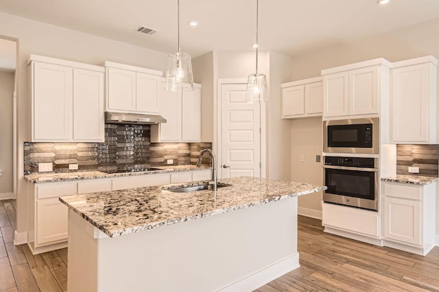 kitchen with a sink, built in microwave, oven, light wood-style floors, and under cabinet range hood