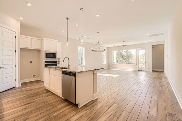 kitchen with a sink, light wood-type flooring, white cabinets, baseboards, and appliances with stainless steel finishes