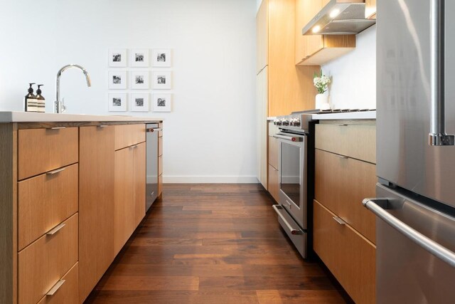 kitchen featuring appliances with stainless steel finishes, light countertops, baseboards, under cabinet range hood, and dark wood-style floors