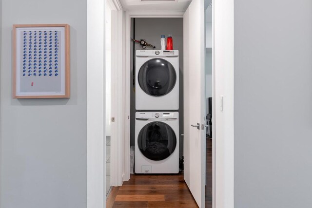 washroom with stacked washer / drying machine, wood finished floors, and laundry area