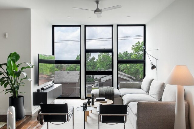 living area featuring plenty of natural light, ceiling fan, wood finished floors, and a wall of windows