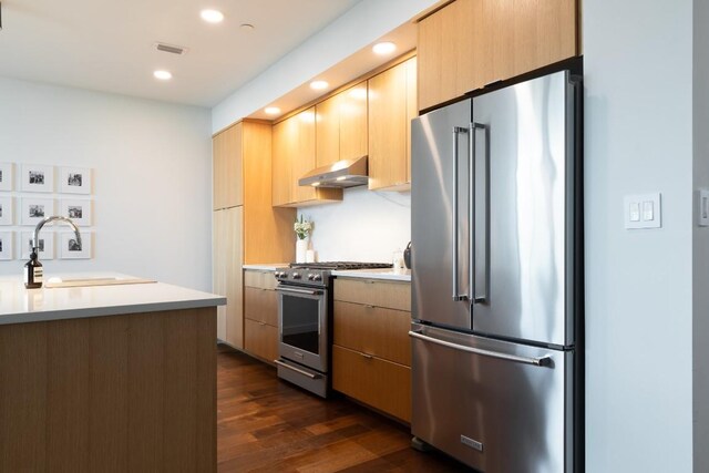 kitchen featuring light countertops, under cabinet range hood, premium appliances, and dark wood-type flooring