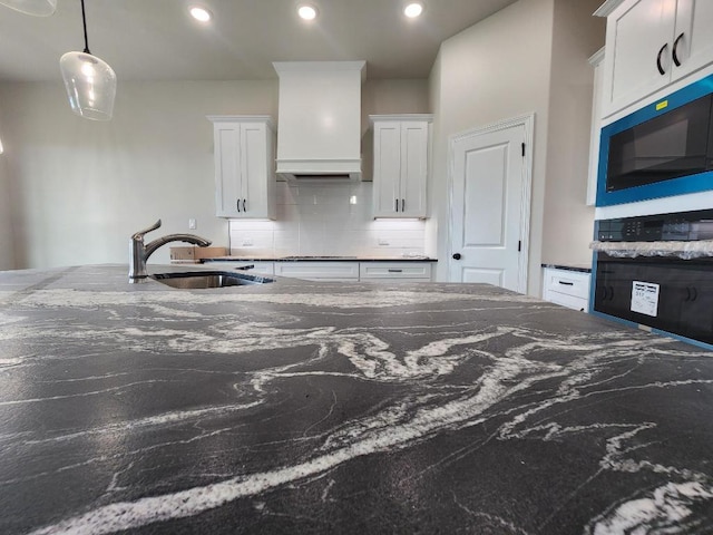 kitchen featuring white cabinets, built in microwave, a sink, and premium range hood
