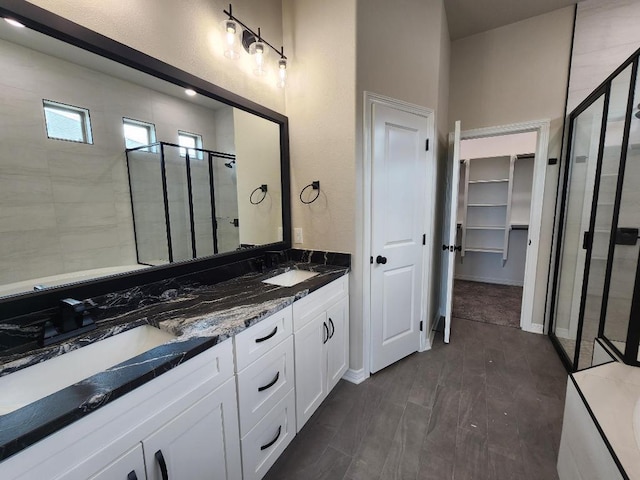 full bath with a sink, a spacious closet, double vanity, and a stall shower