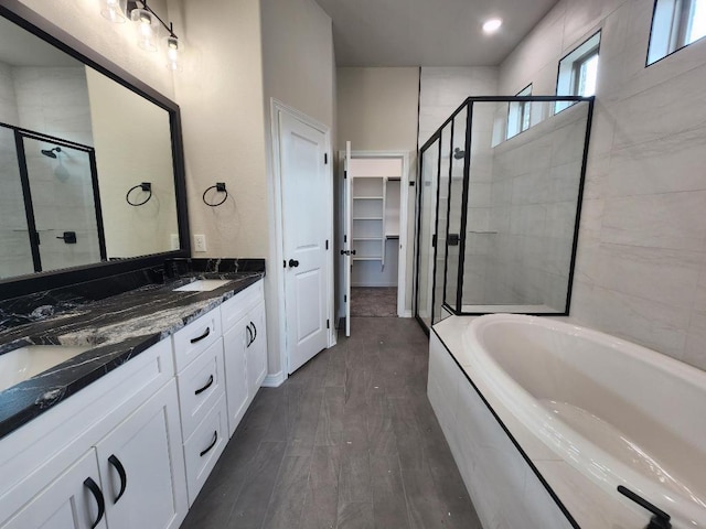 bathroom with double vanity, a shower stall, a garden tub, and a spacious closet