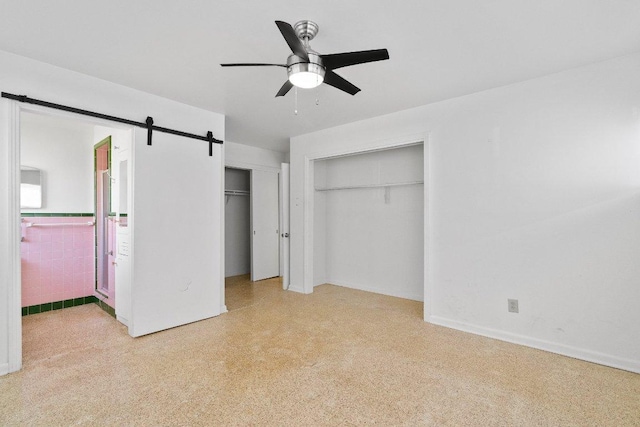unfurnished bedroom with two closets, a barn door, ensuite bath, and a ceiling fan