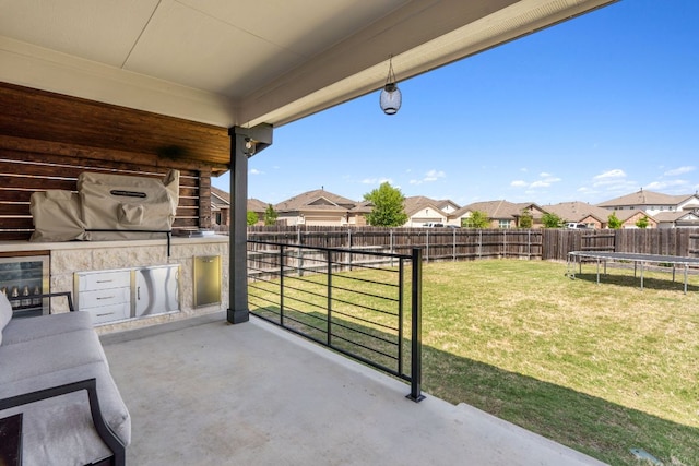 view of patio with beverage cooler, a trampoline, a fenced backyard, an outdoor kitchen, and a residential view