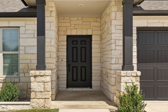 view of exterior entry featuring stone siding and a shingled roof