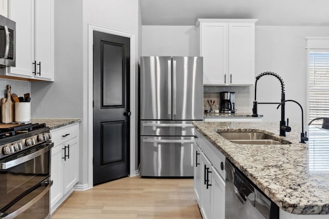 kitchen with light wood finished floors, a sink, appliances with stainless steel finishes, and tasteful backsplash