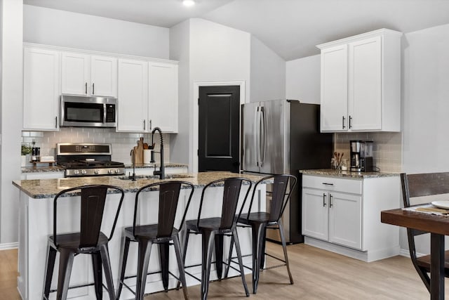 kitchen with stainless steel appliances, backsplash, a sink, light wood-style floors, and dark stone counters