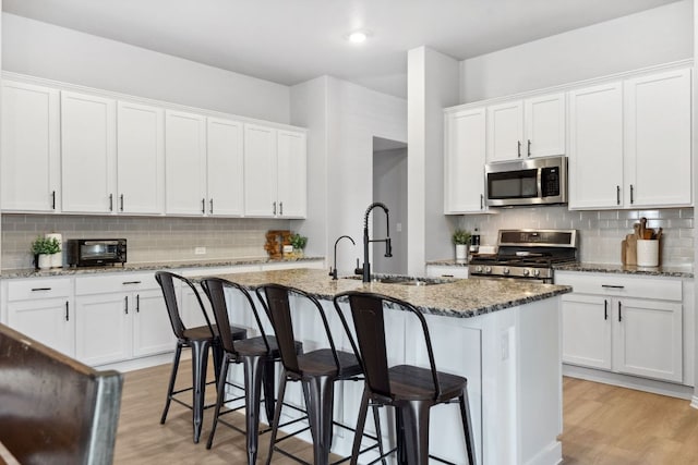 kitchen with light wood-style floors, tasteful backsplash, appliances with stainless steel finishes, and a sink