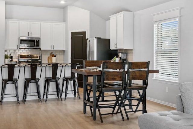 kitchen with white cabinets, a kitchen breakfast bar, stainless steel microwave, gas stove, and tasteful backsplash