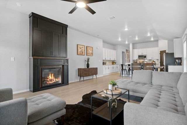 living room featuring light wood finished floors, baseboards, visible vents, ceiling fan, and a fireplace