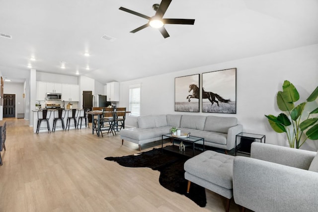 living area with lofted ceiling, a ceiling fan, visible vents, and light wood-type flooring