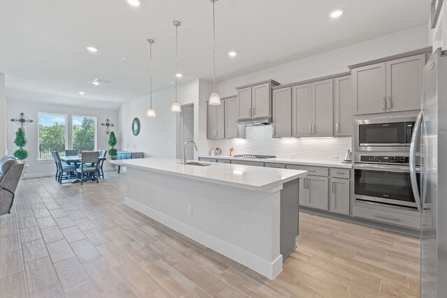 kitchen with a sink, backsplash, gray cabinets, light countertops, and appliances with stainless steel finishes