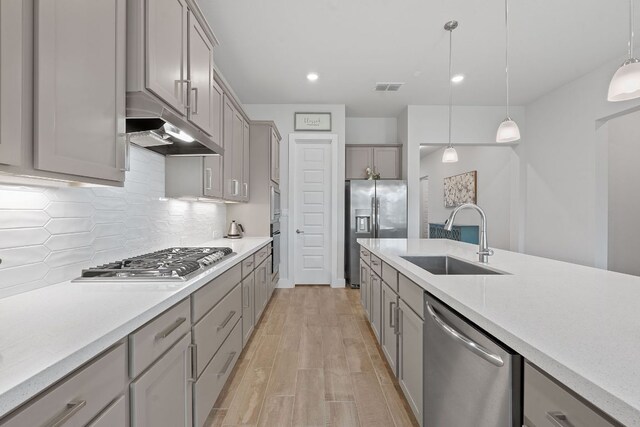 kitchen with stainless steel appliances, a sink, gray cabinetry, light countertops, and under cabinet range hood