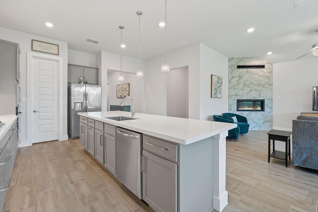 kitchen with a sink, open floor plan, gray cabinets, wood finish floors, and appliances with stainless steel finishes