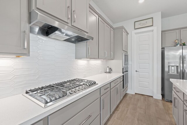 kitchen with stainless steel appliances, gray cabinetry, under cabinet range hood, and light countertops