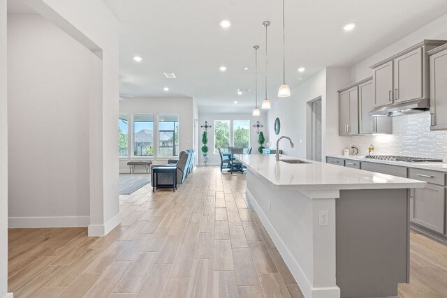 kitchen with light countertops, under cabinet range hood, a sink, and gray cabinets