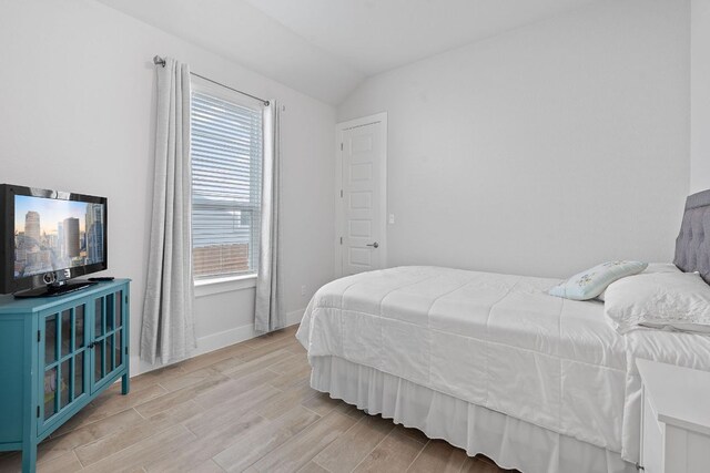 bedroom with light wood-type flooring, vaulted ceiling, and baseboards