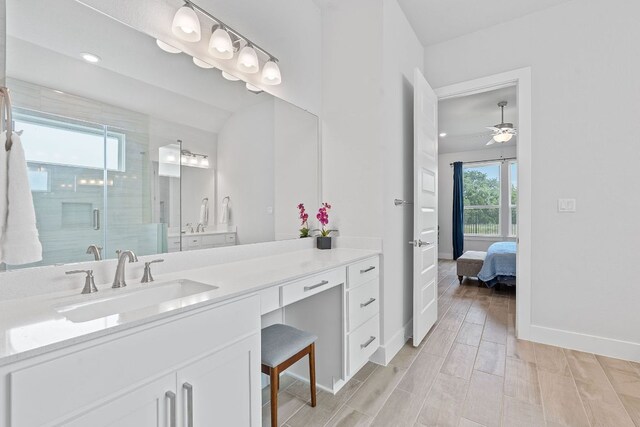 ensuite bathroom featuring a stall shower, baseboards, wood finished floors, ceiling fan, and vanity