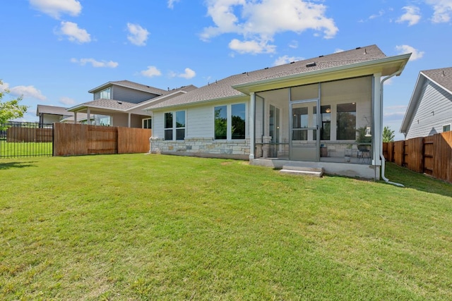back of property with stone siding, a fenced backyard, a sunroom, and a yard