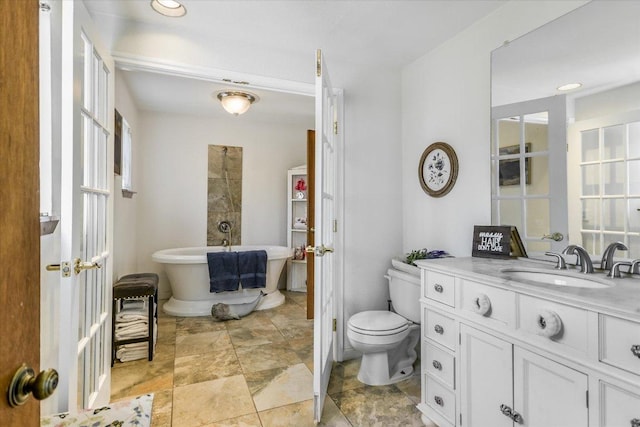 bathroom with a soaking tub, vanity, stone finish floor, and toilet