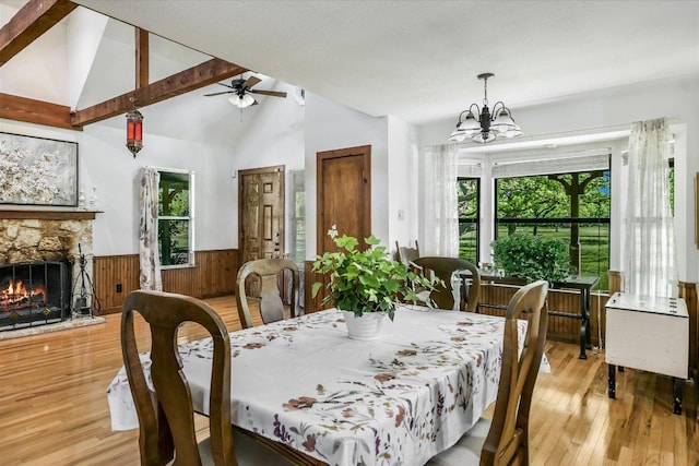 dining space featuring ceiling fan with notable chandelier, wooden walls, a wainscoted wall, light wood finished floors, and a fireplace