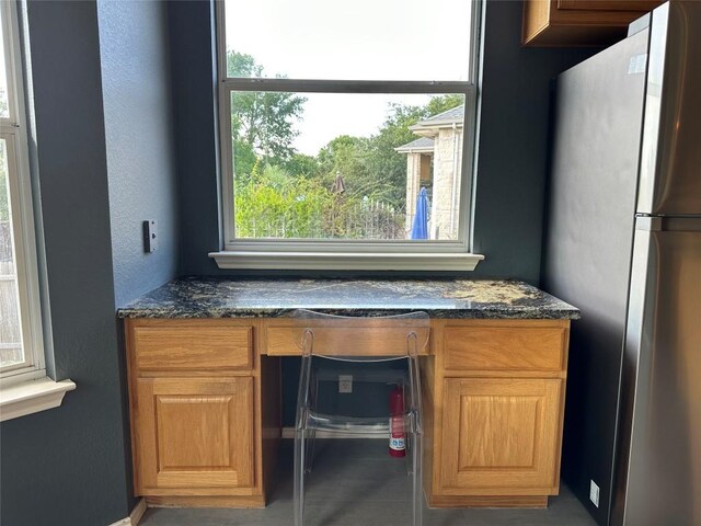 interior details featuring freestanding refrigerator, brown cabinets, dark stone counters, and built in study area