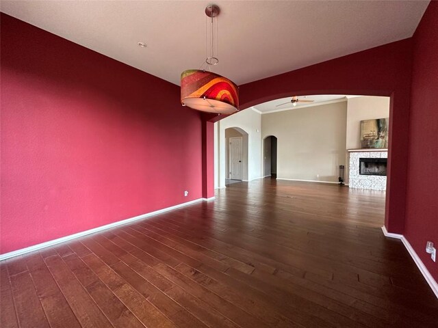 interior space featuring a ceiling fan, wood finished floors, arched walkways, a fireplace, and baseboards