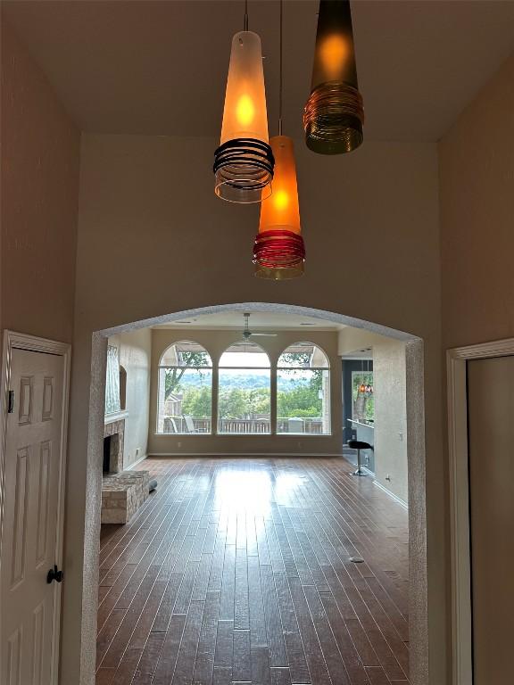 unfurnished living room with arched walkways, dark wood-style flooring, baseboards, a fireplace with raised hearth, and a high ceiling
